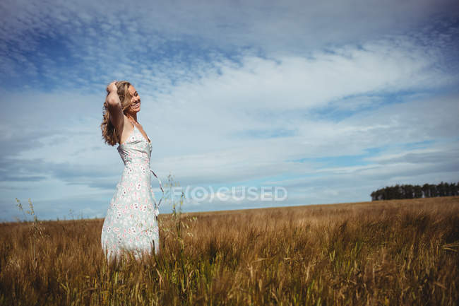 Mulher com a mão no cabelo em pé no campo de trigo no dia ensolarado — Fotografia de Stock