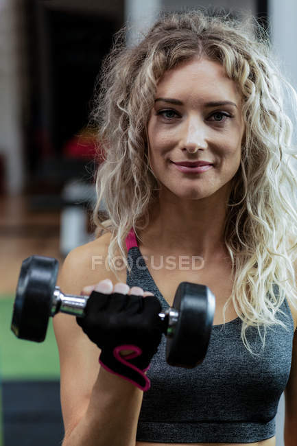 Portrait of beautiful woman lifting dumbbell at gym — Stock Photo