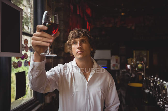 Barista guardando un bicchiere di vino rosso al bancone del bar — Foto stock