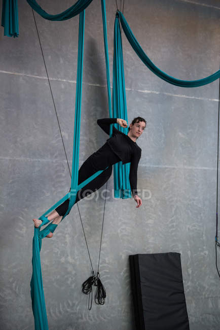 Gymnaste féminine faisant de l'exercice sur corde en tissu bleu dans un studio de fitness — Photo de stock