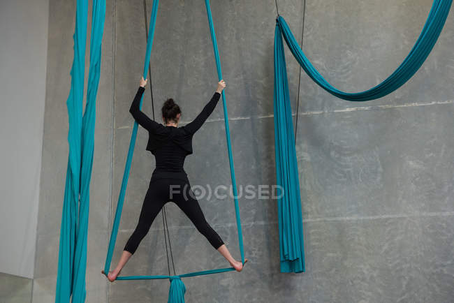 Gimnasta femenina ejercitándose sobre una cuerda de tela azul en un gimnasio - foto de stock