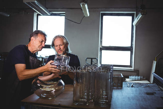 Стеклодув и его коллега рассматривают изделия из стекла на стекольном заводе — стоковое фото