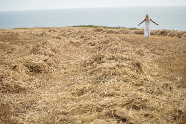 Rückansicht einer unbeschwerten blonden Frau, die in Flussnähe auf einem Feld spaziert — Stockfoto