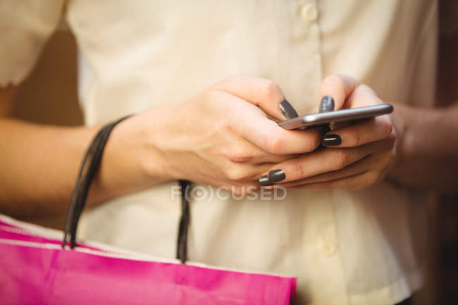Средняя секция женщины, использующей мобильный телефон во время покупок в бутик-магазине — стоковое фото