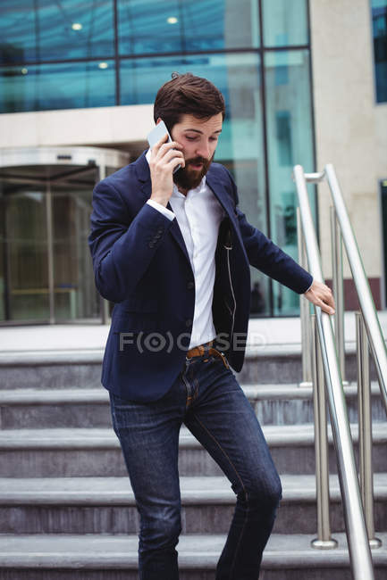 Businessman talking on mobile phone while walking on stairs — Stock Photo