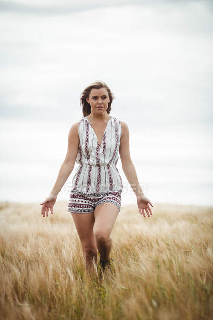 Beautiful woman walking through wheat field on sunny day — Stock Photo