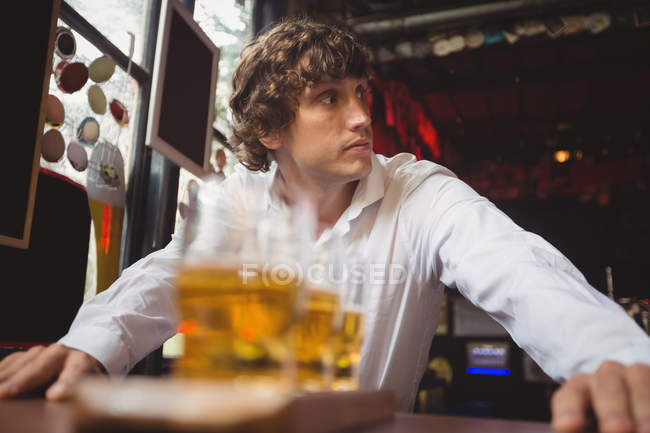 Camarero de pie cerca del mostrador con vasos de cerveza en el bar - foto de stock