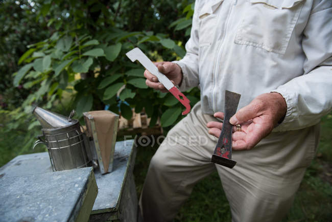 Milieu de l'apiculteur tenant son équipement près de la ruche — Photo de stock