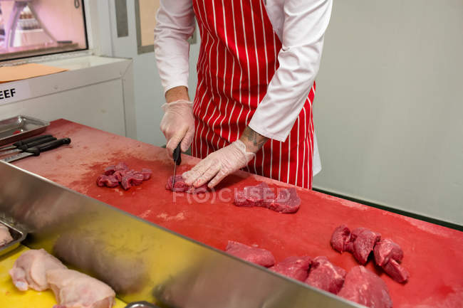 Середня частина м'ясника рубає червоне м'ясо в м'ясному магазині — стокове фото