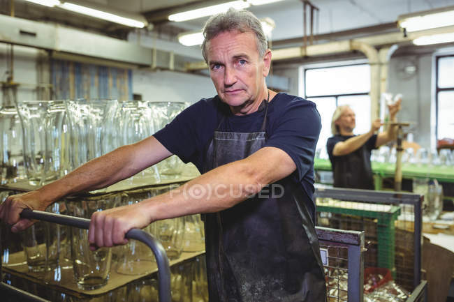 Retrato del soplador de vidrio empujando un carro en la fábrica de soplado de vidrio - foto de stock
