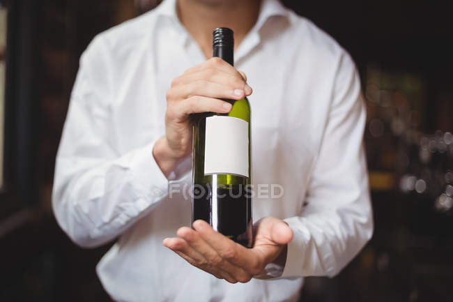 Sección media de la barra de licitación sosteniendo una botella de vino en el bar - foto de stock