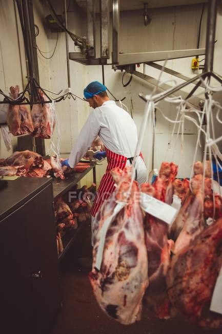 Açougueiro trabalhando na sala de armazenamento de carne no açougue — Fotografia de Stock