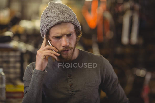 Mecânico falando no telefone celular na loja de bicicletas — Fotografia de Stock