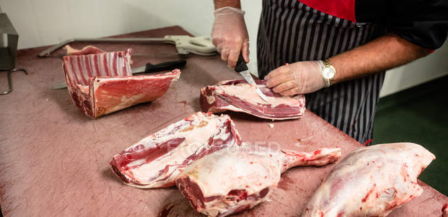 Средняя часть мясника режет рёбра туши свинины в мясной лавке — стоковое фото