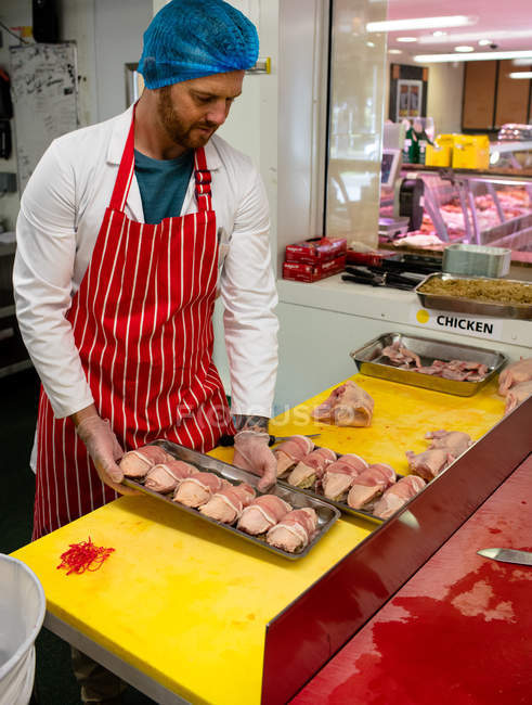 Macellaio che tiene un vassoio di pollo e rotoli di bistecca in macelleria — Foto stock