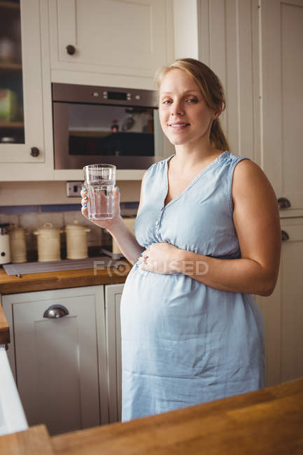 Porträt einer schwangeren Frau, die zu Hause in der Küche Wasser trinkt — Stockfoto