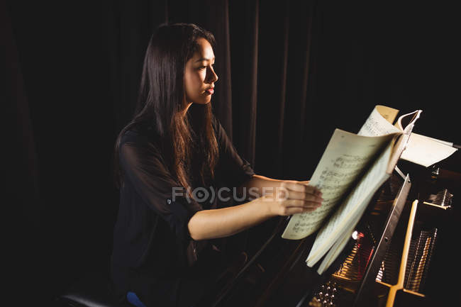 Estudante feminina olhando para partituras enquanto toca piano em um estúdio — Fotografia de Stock