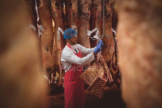 М'ясник висить червоне м'ясо в сховищі в м'ясному магазині — стокове фото