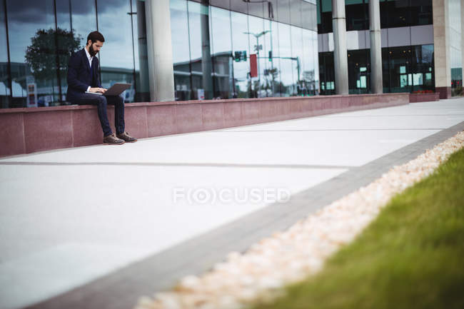 Empresário sentado na passagem do prédio de escritórios e usando laptop — Fotografia de Stock