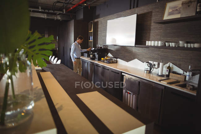 Бизнесмен готовит кофе в кофеварке в столовой — стоковое фото