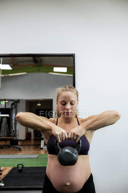 Femme enceinte levant cloche bouilloire dans la salle de gym — Photo de stock