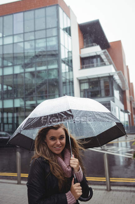 Portrait of beautiful woman holding umbrella during rainy season on street — Stock Photo