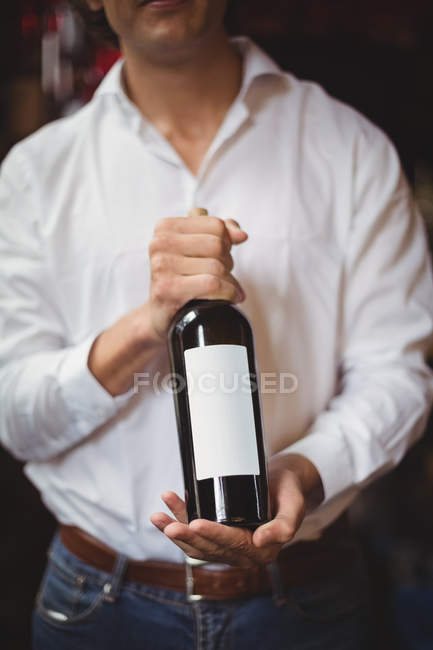 Sección media de la barra de licitación sosteniendo una botella de vino en el bar - foto de stock