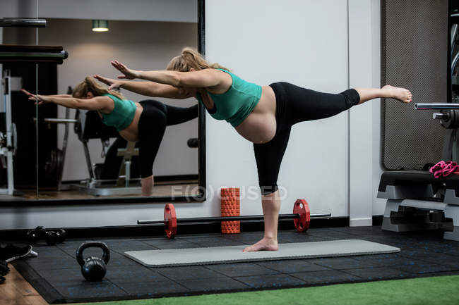 Вагітна жінка, виконуючи розтяжку вправи на тренувальному килимку в тренажерному залі — стокове фото