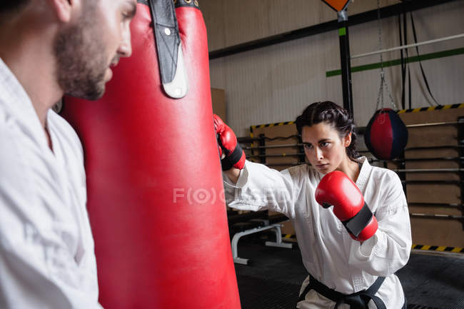 Selective focus of sportswoman and sportsman practicing karate with punching bag in studio — Stock Photo