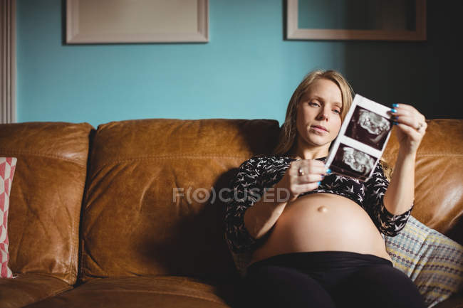 Mujer embarazada mirando la ecografía en la sala de estar en casa - foto de stock