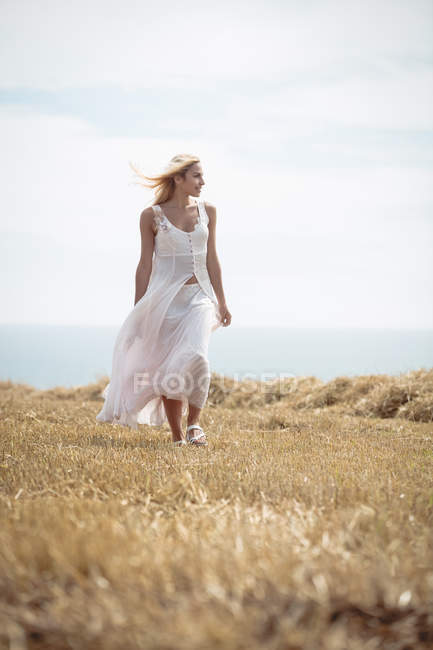 Beautiful blonde woman walking in field near river — Stock Photo