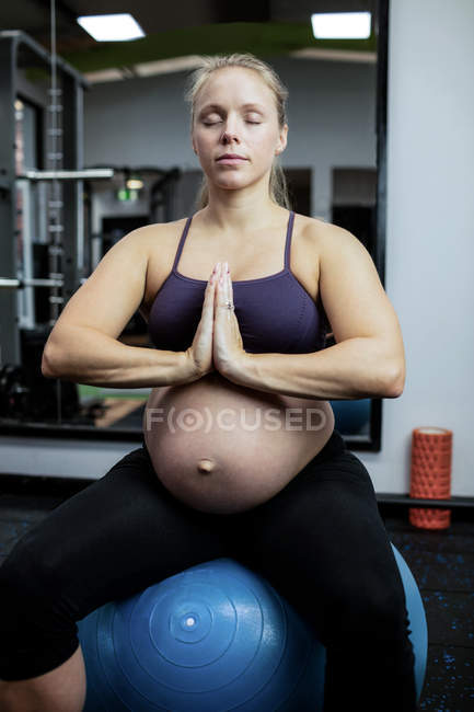Mujer embarazada realizando yoga sobre pelota de fitness en gimnasio - foto de stock