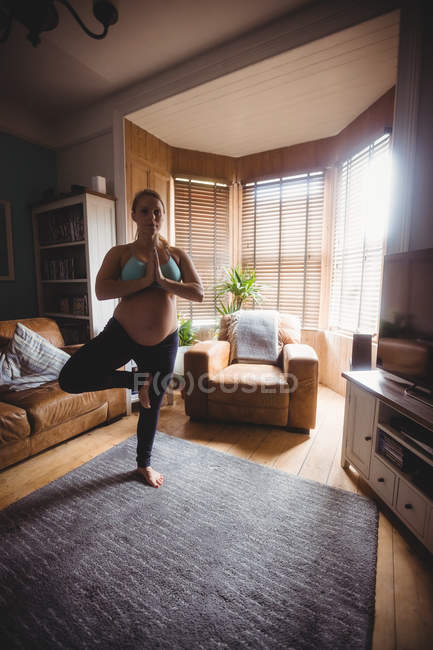 Femme enceinte effectuant du yoga dans le salon à la maison — Photo de stock