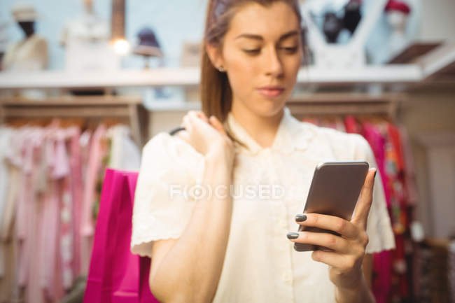 Mujer usando el teléfono móvil mientras hace compras en la tienda boutique - foto de stock
