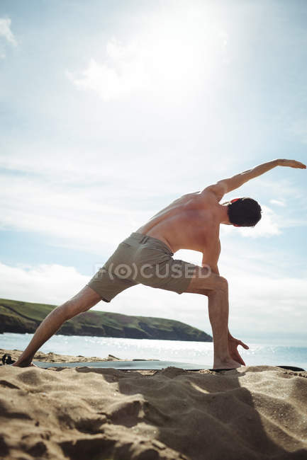 Задний вид человека, выполняющего упражнения на растяжку на пляже — стоковое фото