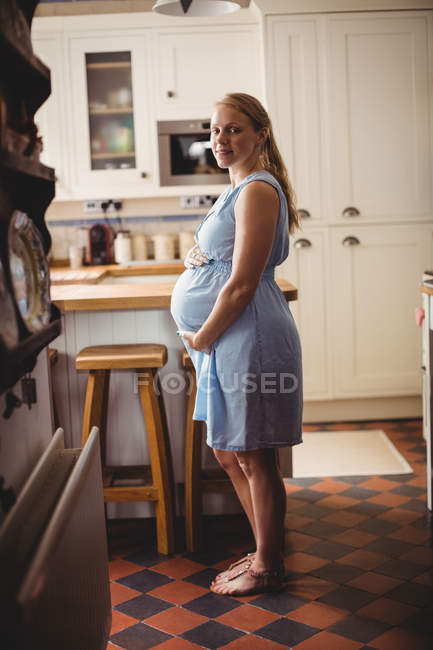 Вид сбоку на портрет беременной женщины, стоящей на кухне дома — стоковое фото