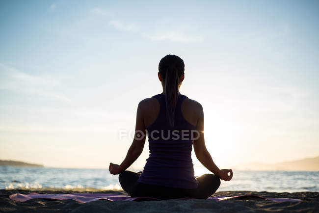 Вид ззаду жінка практикує йогу на пляжі в сонячний день — стокове фото