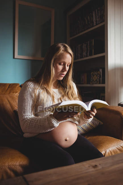 Pregnant woman reading book in living room at home — Stock Photo
