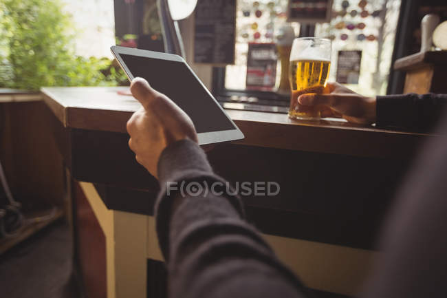 Homem usando tablet digital com copo de cerveja na mão no bar — Fotografia de Stock