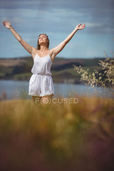 Mujer de pie en el campo con las manos levantadas - foto de stock
