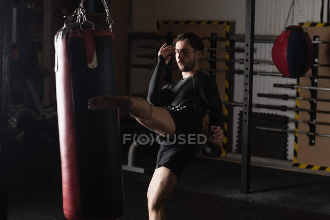 Boxer masculino praticando boxe com saco de perfuração no estúdio de fitness — Fotografia de Stock