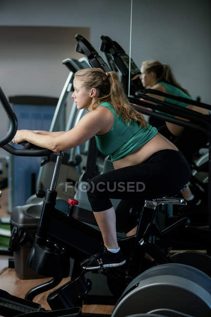 Femme enceinte travaillant sur vélo d'appartement à la salle de gym — Photo de stock