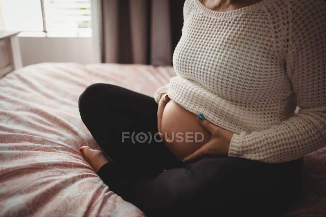 Midsection de la femme enceinte se détendre dans la chambre à coucher à la maison — Photo de stock