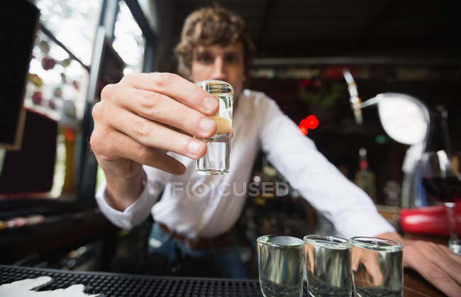 Ritratto del barista che tiene il bicchiere di tequila al bancone del bar nel bar — Foto stock