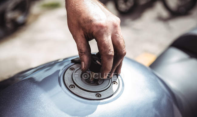 Hand of mechanic closing fuel tank of motor bike at workshop — Stock Photo