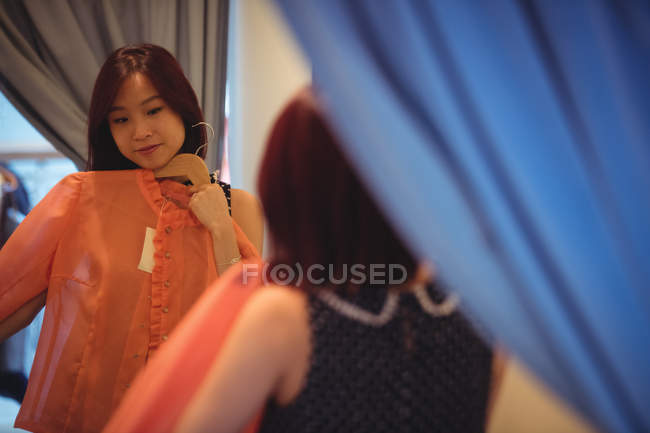 Frau schaut in Spiegel, während sie in Boutique-Geschäft ein Oberteil probiert — Stockfoto