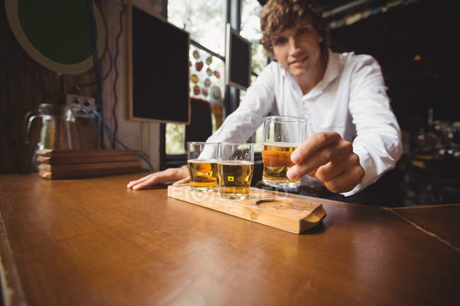 Retrato del camarero sosteniendo vaso de whisky en el mostrador del bar en el bar - foto de stock