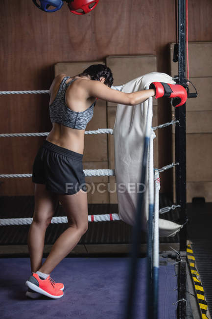 Back view of Tired boxer in boxing gloves leaning on ropes of boxing ring at fitness studio — Stock Photo