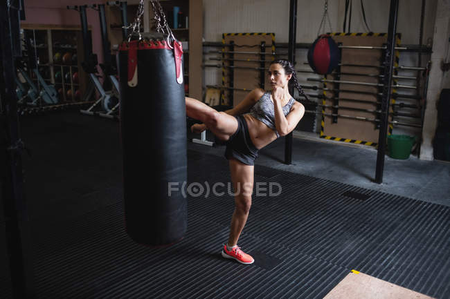 Vista de alto ângulo do boxer feminino chutando saco de perfuração no estúdio de fitness — Fotografia de Stock