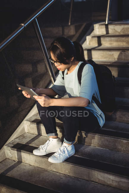 Mujer joven sentada en la escalera y usando tableta digital por la noche - foto de stock